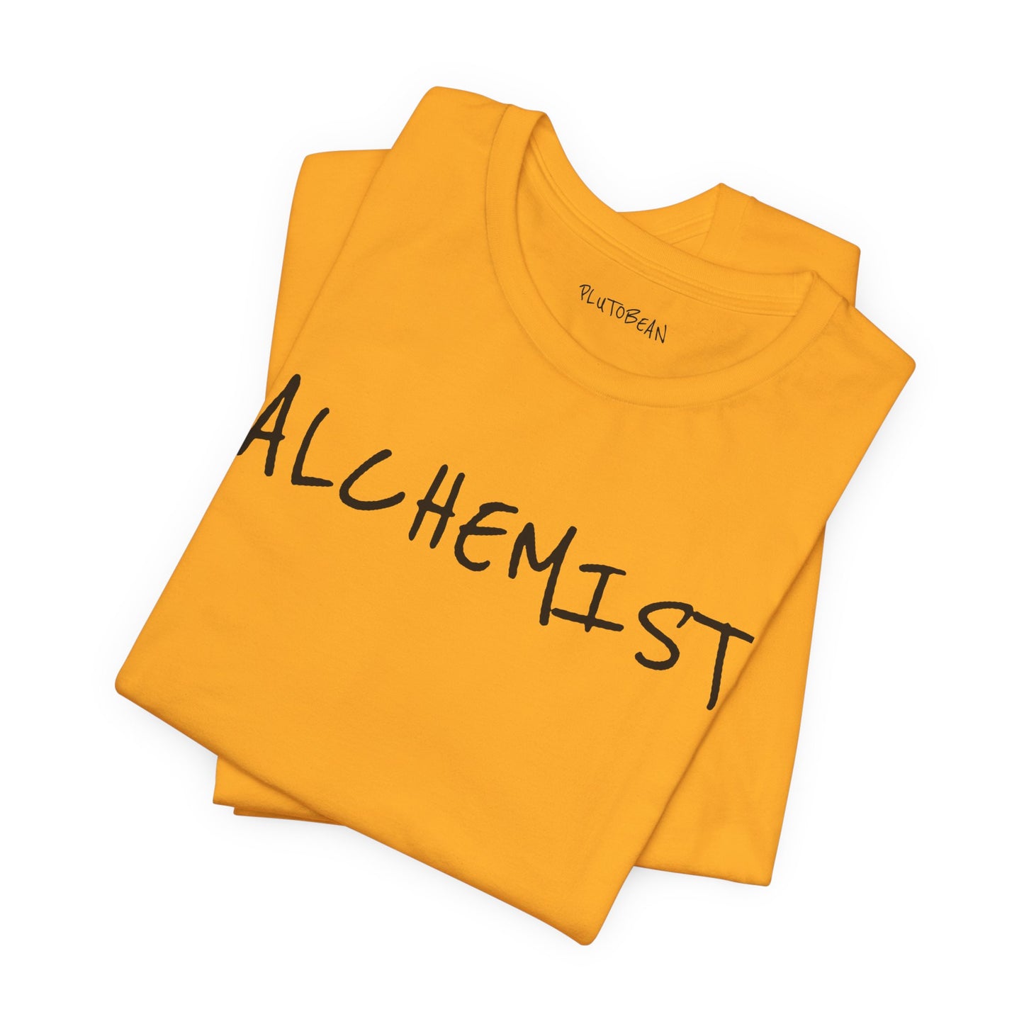 Folded gold tee with bold handwritten “ALCHEMIST” wordmark in black