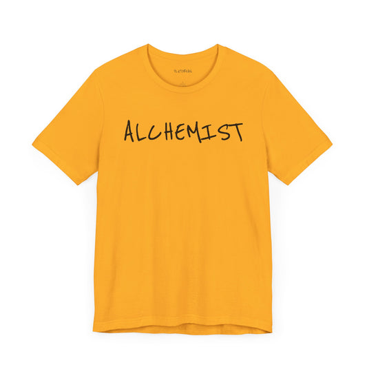Gold t-shirt with handwritten black “ALCHEMIST” text across the chest