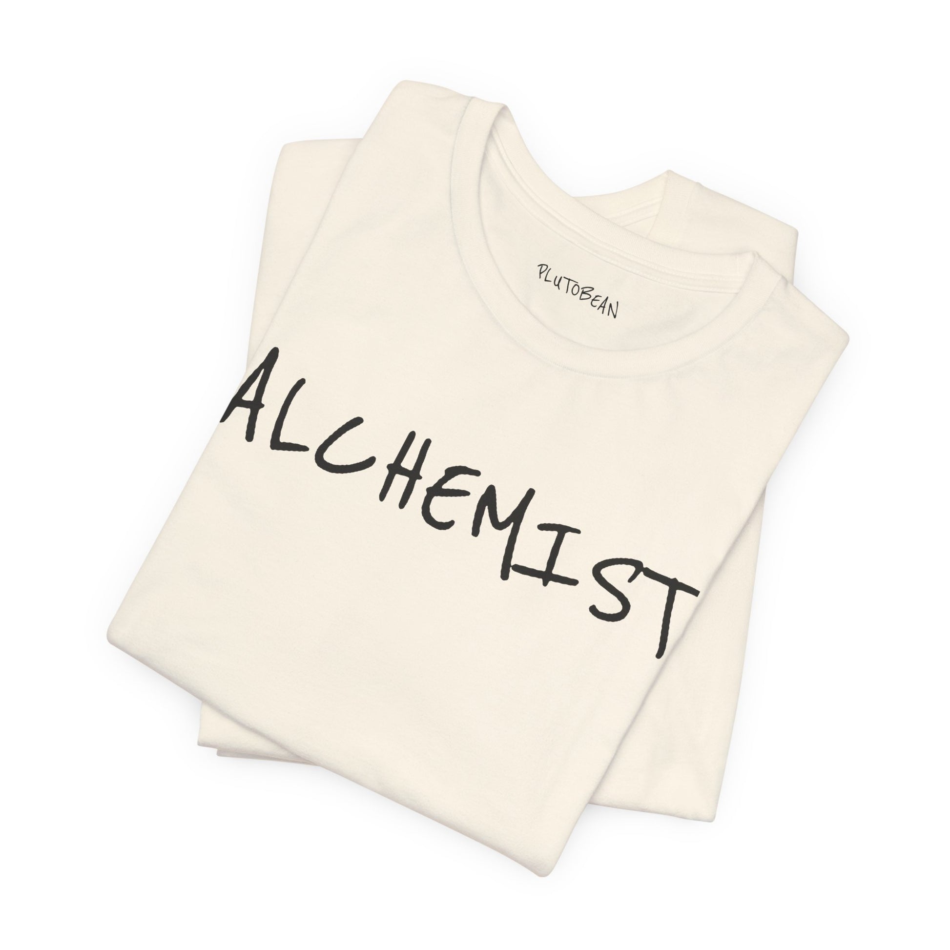 Folded natural tee with bold handwritten “ALCHEMIST” wordmark in black